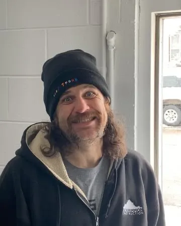 Bryan Youngs, coach at Denver Thai Boxing, smiling in a beanie and hoodie inside the gym.